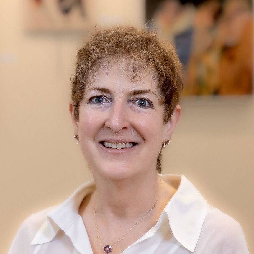 Smiling woman with curly short hair in a white shirt.